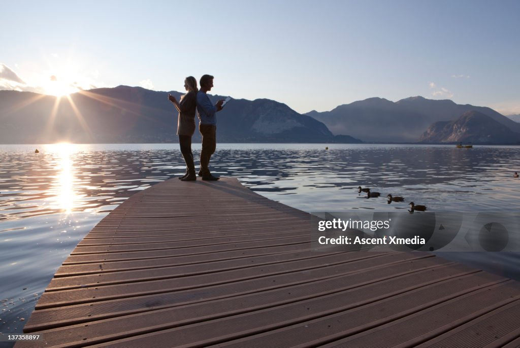 Couple use tablet computer/cell phone on lake wahrf, sunrise