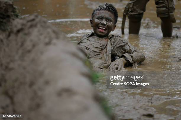 Kid smiles while playing in muddy paddy fields to commemorate Asar Pandra, also known as National Paddy Day, which signifies the commencement of rice...