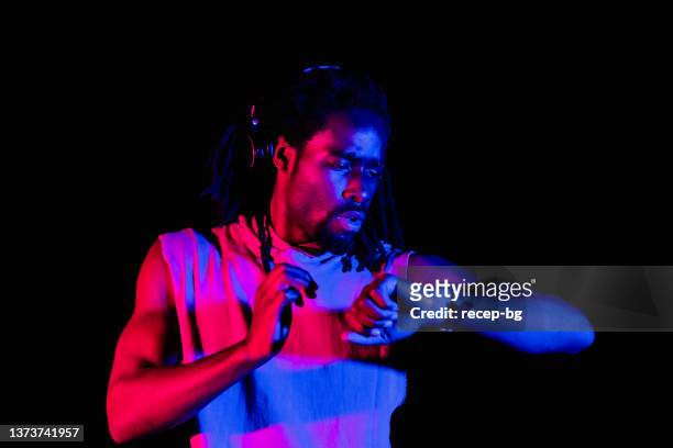 black-ethnic sports person running at night in city. he is checking smart watch - locs hairstyle stock pictures, royalty-free photos & images
