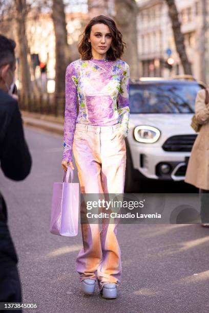 Mary Leest poses ahead of the MSGM fashion show wearing a pink printed sheer top, orange and pink tie dye jeans, lilac bag and lilac platform heels...