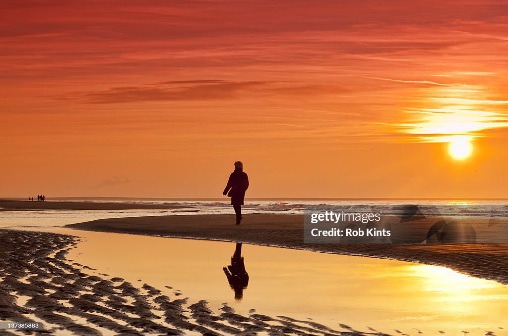 Silhouette of woman walking on beach at sunset