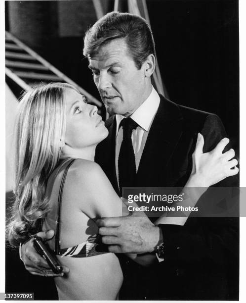 Roger Moore holds a gun as he embraces Britt Ekland who is wearing a bikini top in a scene from the film 'The Man With The Golden Gun', 1974.