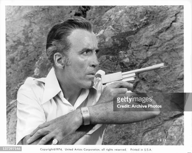 Christopher Lee along side a cliff wall pointing a gun in a scene from the film 'The Man With The Golden Gun', 1974.