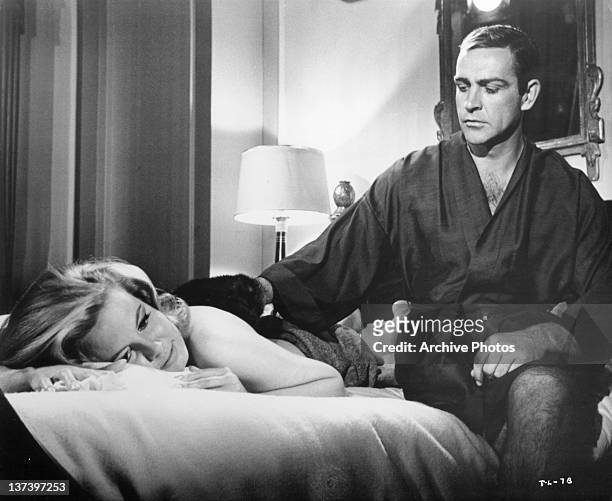 Molly Peters getting her back rubbed by Sean Connery who is wearing a robe in a scene from the film 'Thunderball', 1965.