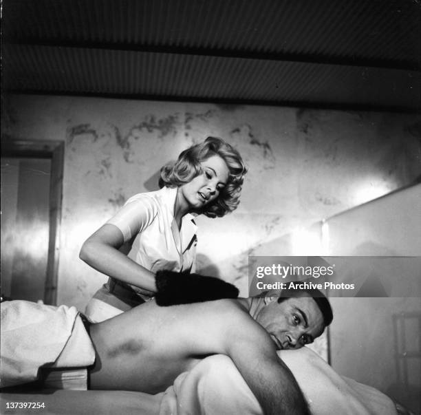 Molly Peters rubs Sean Connery back with a fur mitten in a scene from the film 'Thunderball', 1965.
