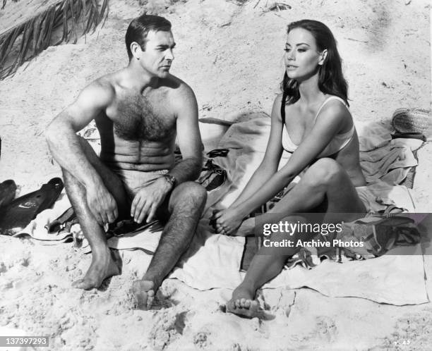 Sean Connery watches Claudine Auger clutch her foot after having stepped on a poisonous sea egg spine in a scene from the film 'Thunderball', 1965.