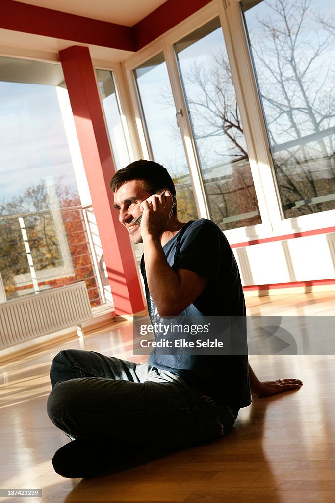 Man sitting in new apartment phoning and smiling