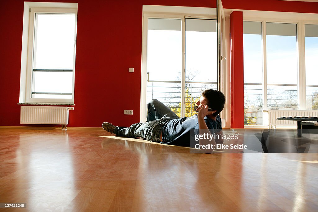 Man laying in empty apartment phoning