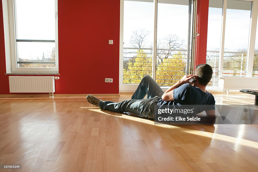 Man laying in new apartment holding mobile phone