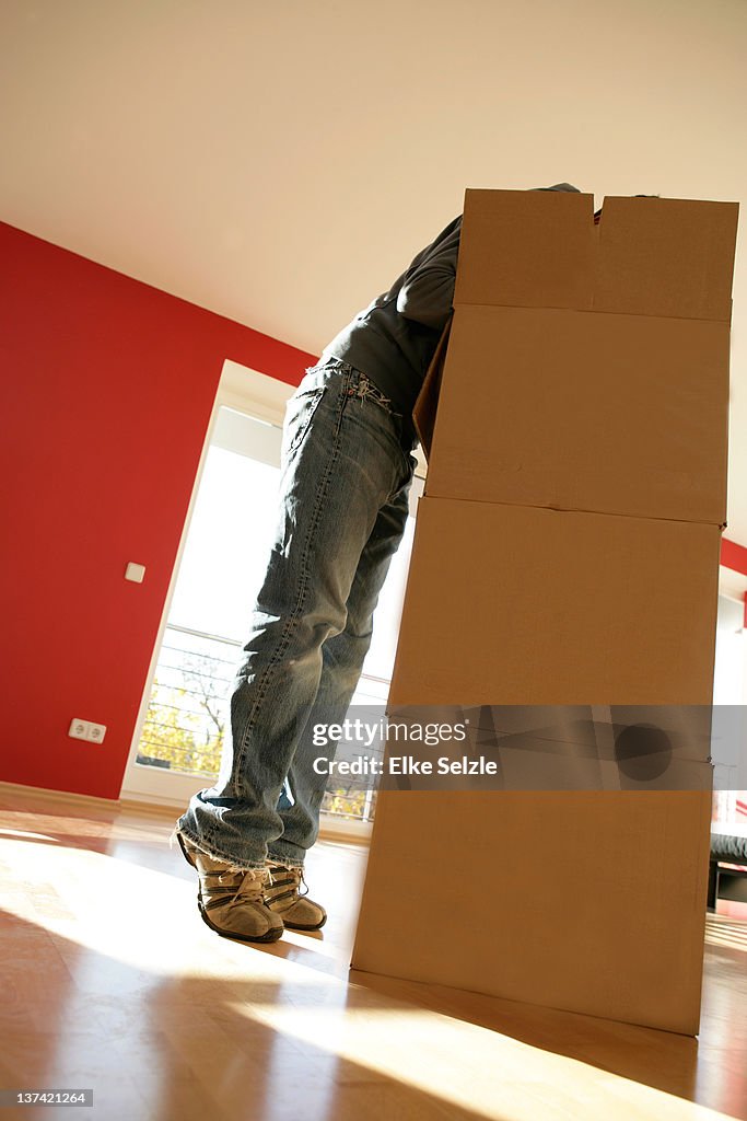 Tiptoeing man bending over boxes in empty apartmen