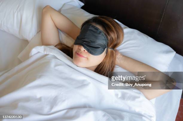 young asian woman wearing sleep mask during sleeping on the bed. - beautiful woman sleeping stock pictures, royalty-free photos & images