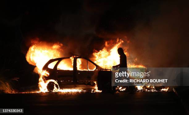 Protester walks by a burning car during clashes with police in Le Port, French Indian Ocean island of La Reunion, on June 30 three days after a...
