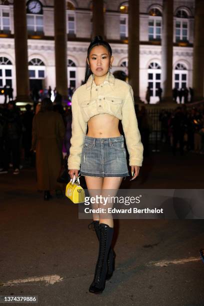 Jaime Xie wears gold earrings, a beige fluffy cropped cargo shirt, a gray faded denim short jeans skirt, a yellow shiny leather with white...