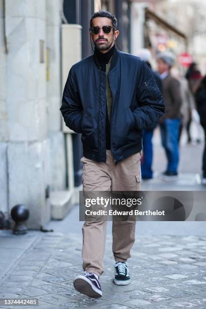 Guest wears black sunglasses from Ray Ban, a black turtleneck pullover, a khaki zipper jacket, a navy blue bomber coat, beige cargo pants, black...