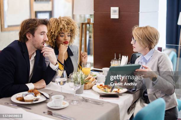 geschäftsleute sprechen über die arbeit, die auf ein digitales tablet schaut, während sie in einem restaurant frühstücken. - breakfast meeting stock-fotos und bilder