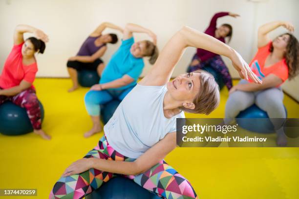 grupo de mujeres sentadas en pelotas de fitness y haciendo ejercicios durante el entrenamiento de pilates - yoga ball fotografías e imágenes de stock