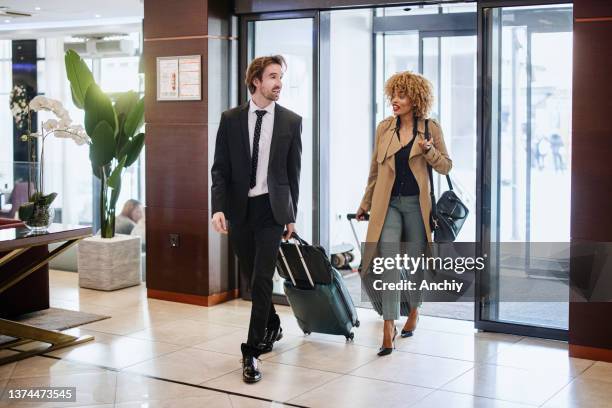 a multiethnic business couple enters a hotel - business woman suitcase stock pictures, royalty-free photos & images