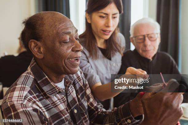 female caregiver teaching senior man knitting in nursing home - public building ストックフォトと画像