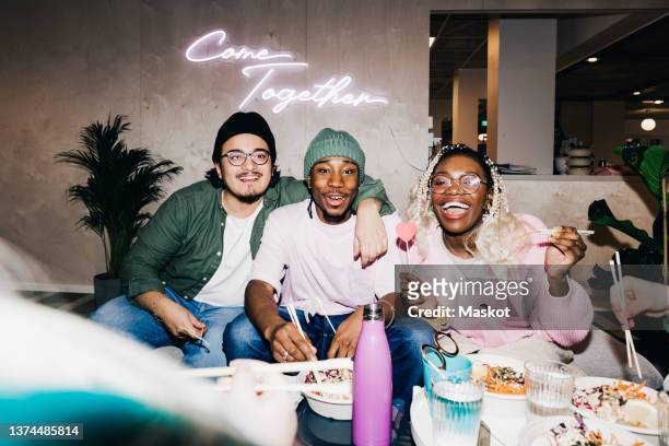 portrait of cheerful multiracial male and female friends enjoying meal in college dorm - college dorm party stock-fotos und bilder