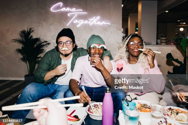 portrait of happy multiracial male and female friends with props having food in college dorm - college dorm party stock-fotos und bilder