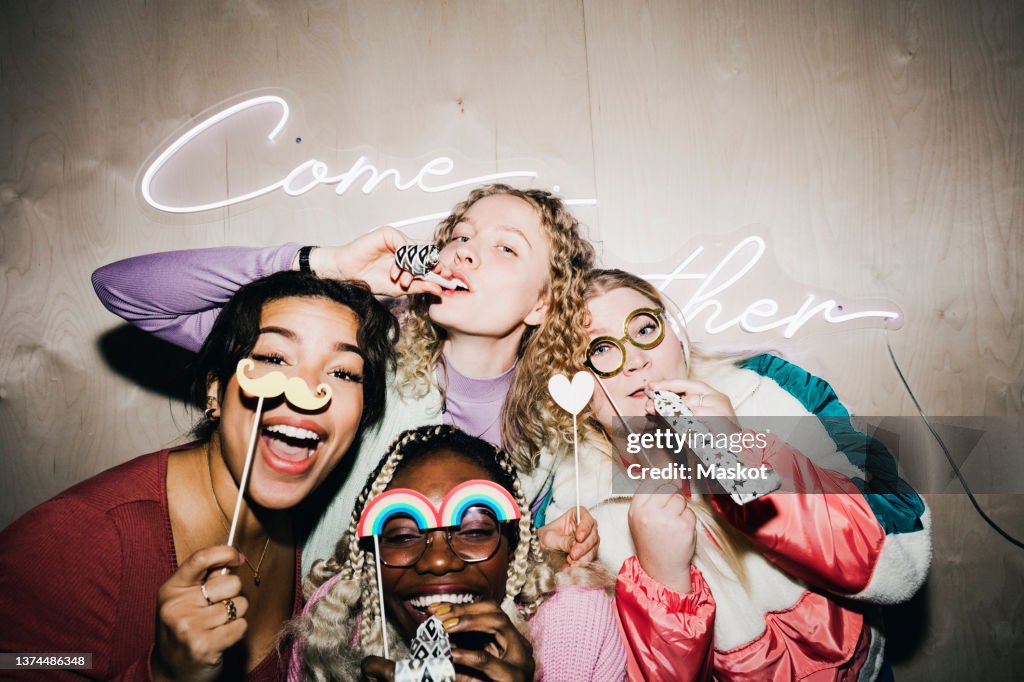 Portrait of carefree multiracial female friends with props enjoying in college dorm