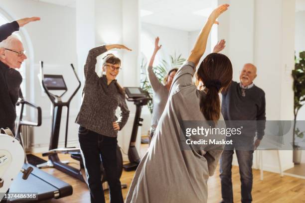 Female caregiver assisting elderly men and women to exercise at nursing home