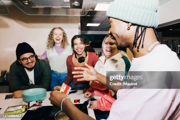 happy multiracial young man and women looking at male friend preparing food in college dorm - preparing food talking stock pictures, royalty-free photos & images