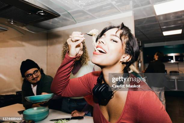 happy young woman eating noodles by friend in kitchen at college dorm - cooking stockfoto's en -beelden