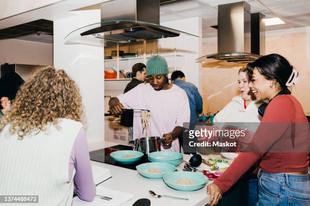 multiracial young man and women with male friend serving noodles in college dorm - room mates male stock-fotos und bilder