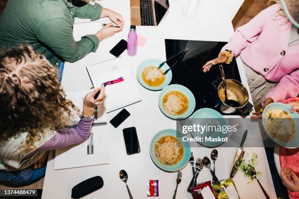 high angle view of multiracial young friends having noodles while studying at dining table in college dorm - college dorm stock pictures, royalty-free photos & images