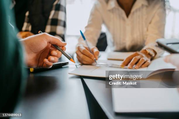 midsection of female student explaining friends at table in university cafeteria - education building stock-fotos und bilder