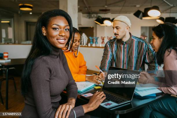 portrait of smiling young woman sitting with friends discussing at college cafeteria - college students diverse stock pictures, royalty-free photos & images