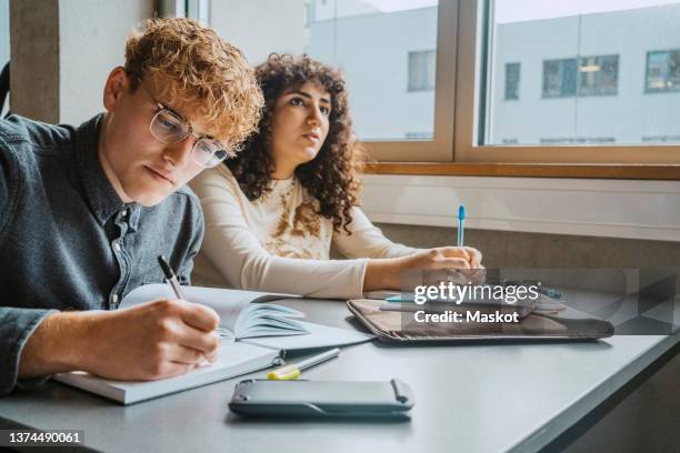 young multiracial male and female students learning in classroom at community college - male student wearing glasses with friends stockfoto's en -beelden