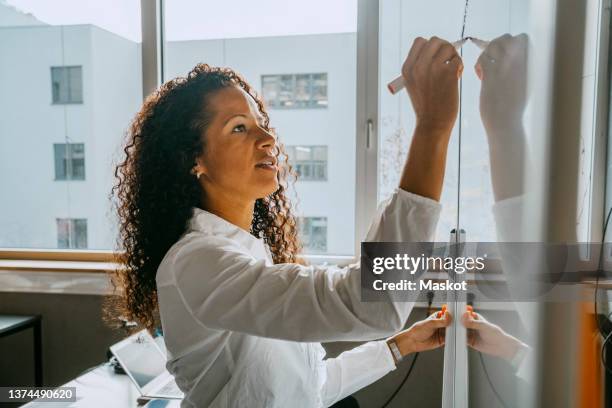 side view of teacher writing on whiteboard with felt tip pen in classroom - profesor fotografías e imágenes de stock