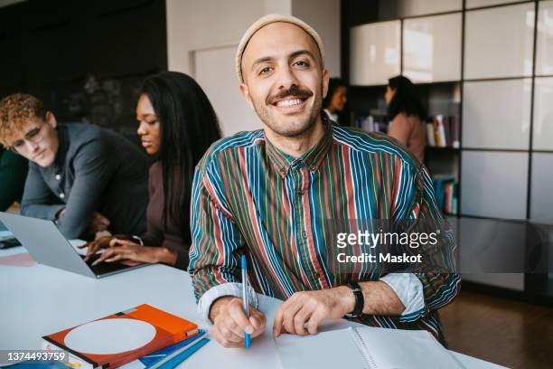 portrait of smiling male student sitting with book at community college - student stock-fotos und bilder