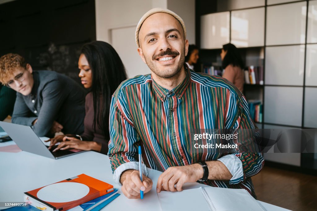 Portrait of smiling male student sitting with book at community college