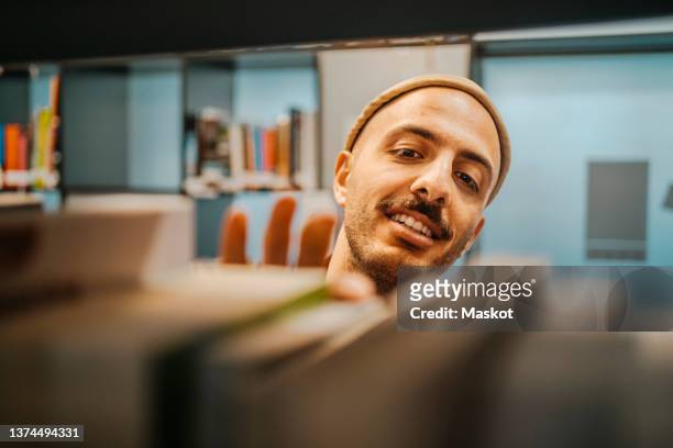 smiling man searching book in library at university - suchen stock-fotos und bilder