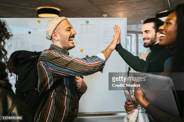 cheerful male friends giving high-five by woman laughing in college - student stock-fotos und bilder