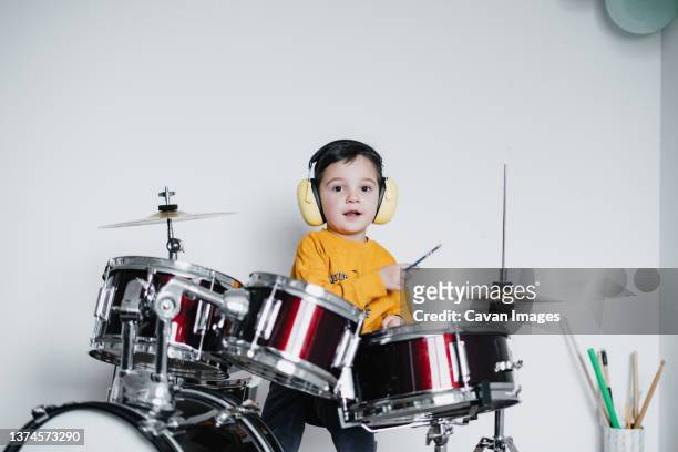 kid wearing ear protective headphones while playing drums - ear drum stockfoto's en -beelden