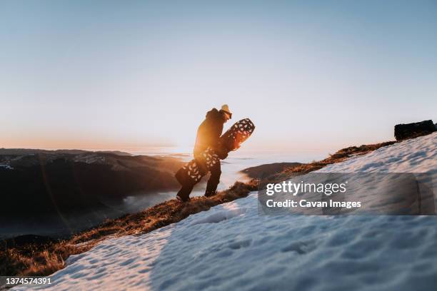 snowboarder in sportswear hiking in the mountains with snowboard - heli skiing stock pictures, royalty-free photos & images