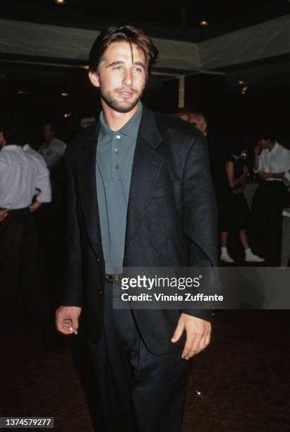 American actor William Baldwin, wearing a black suit with a grey polo shirt, circa 1995.
