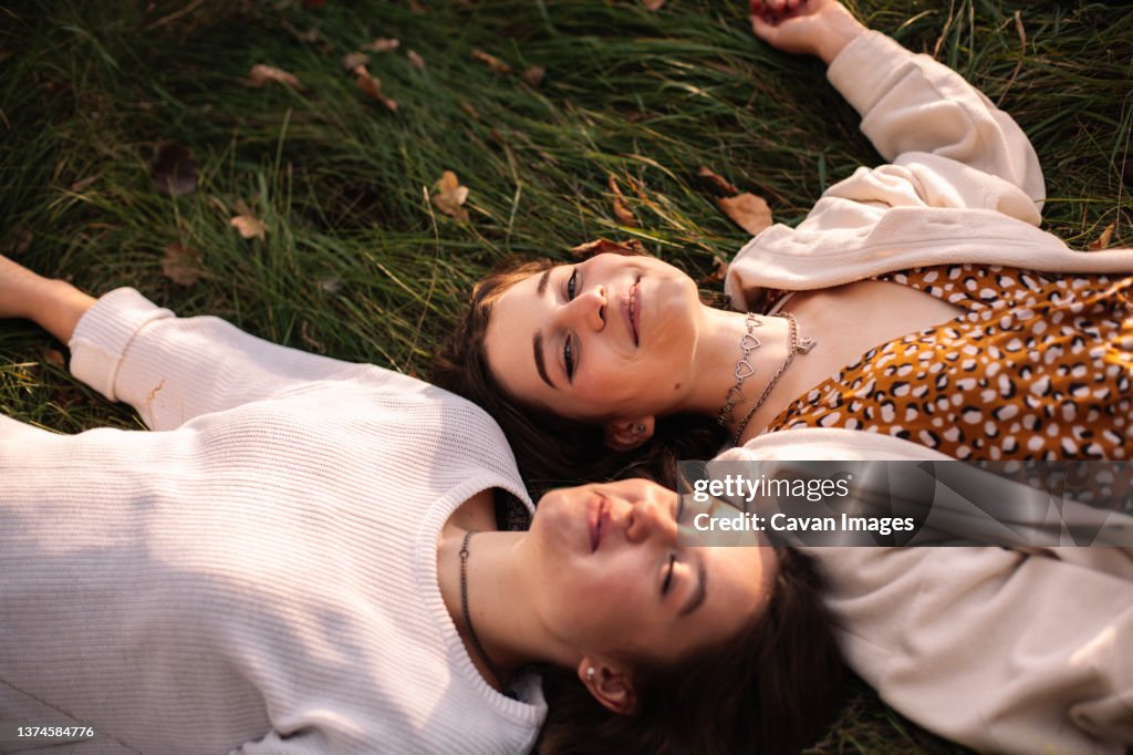 Two happy female friends smiling while lying on grass