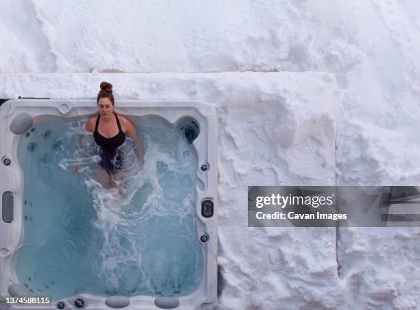 overhead of woman relaxing in hot tub on snow covered deck in winter. - hot tub stock pictures, royalty-free photos & images