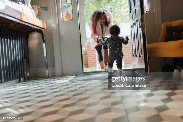 happy mother greeting baby daughter at front door - learning to walk stockfoto's en -beelden