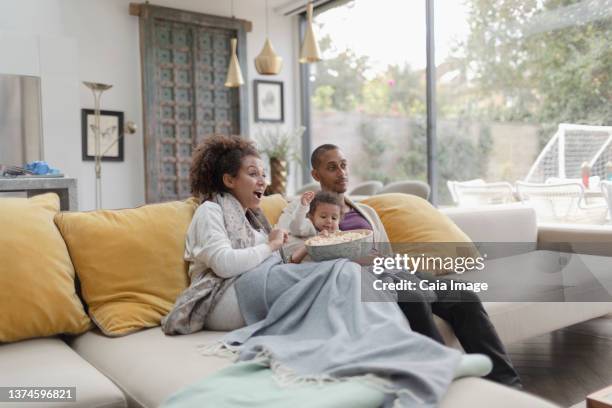family watching movie and eating popcorn on living room sofa - indian living room stock-fotos und bilder