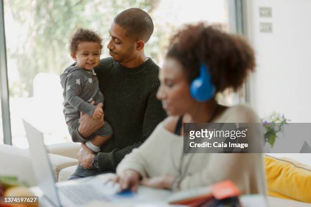 father holding baby daughter behind mother working at laptop - stay home - fotografias e filmes do acervo