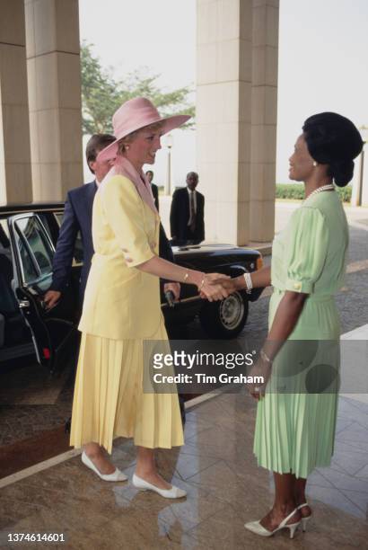 Diana, Princess of Wales , wearing a yellow-and-pink Catherine Walker suit with a pink Philip Somerville hat, shaking hands with a woman during a...