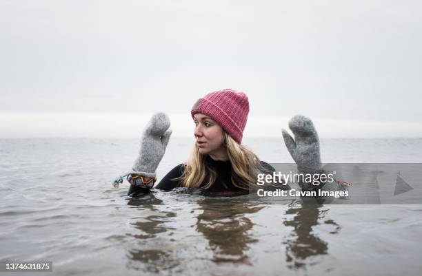 woman breathing cold water swimming with gloves and hat in the ocean - winter strand stock-fotos und bilder