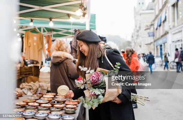 asian woman holding flowers shopping around a market in england - winchester england stock-fotos und bilder