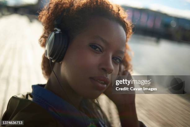 portrait of a young black female with big afro hair wearing headphones - rim light portrait stock pictures, royalty-free photos & images